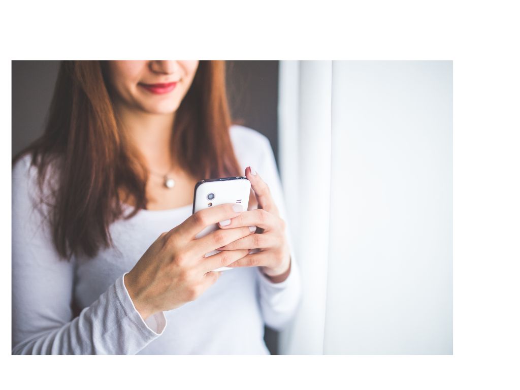 Mulher sorrindo enquanto usa o celular — cliente pesquisando um salão de beleza
